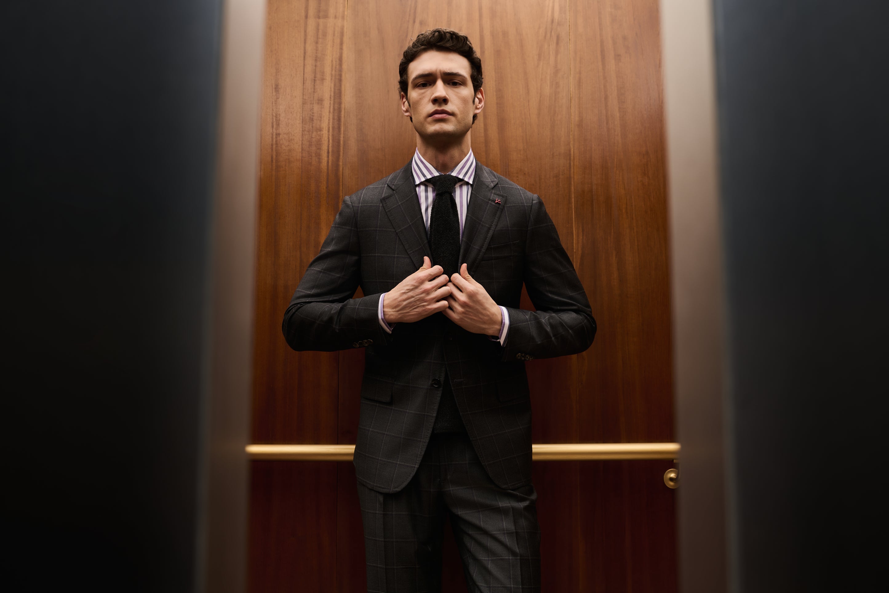 A man in a black and gray plaid suit with a purple shirt and black tie.