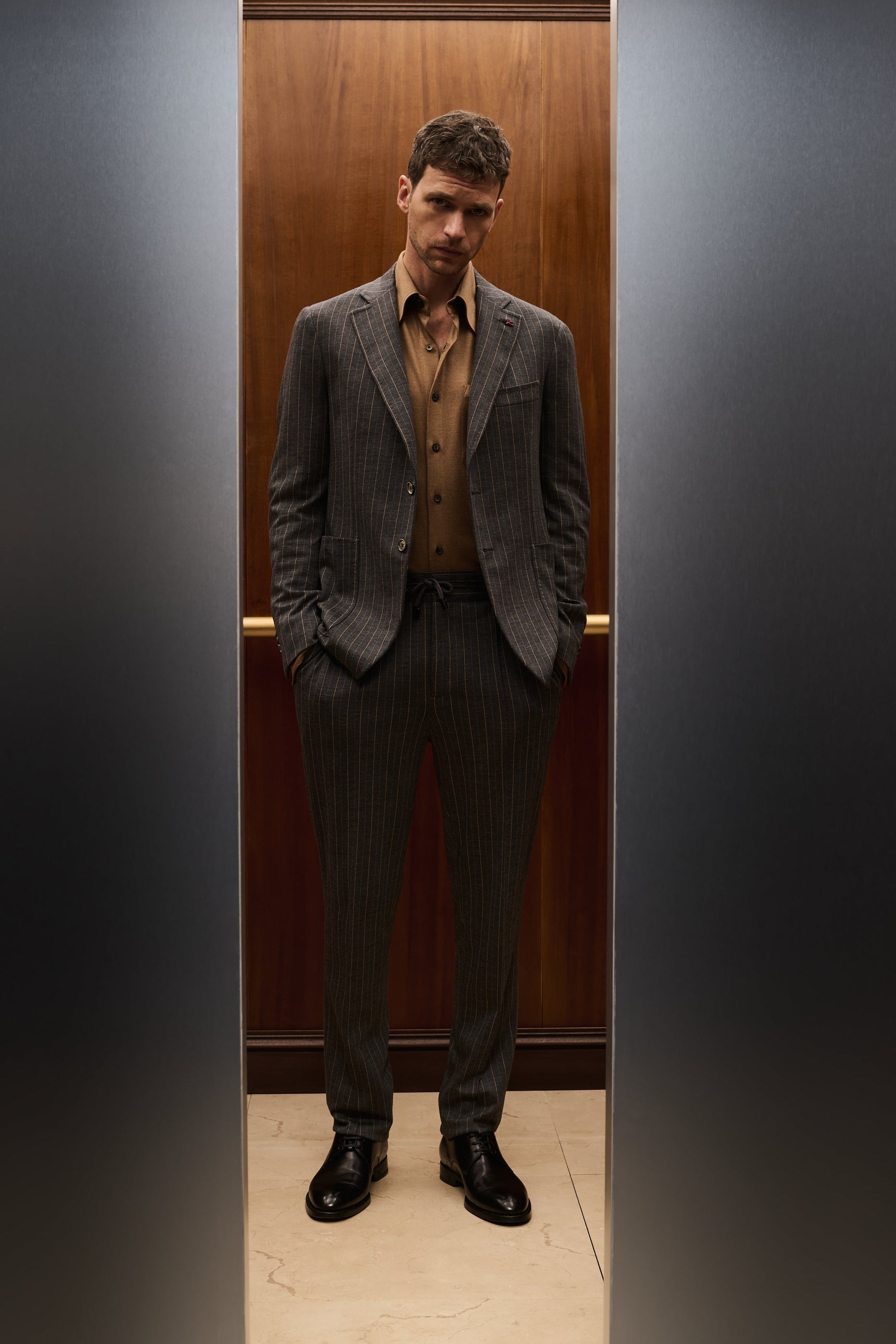 ISAIA Made to Measure: grey pinstripe suit with brown shirt, framed by the elevator doors