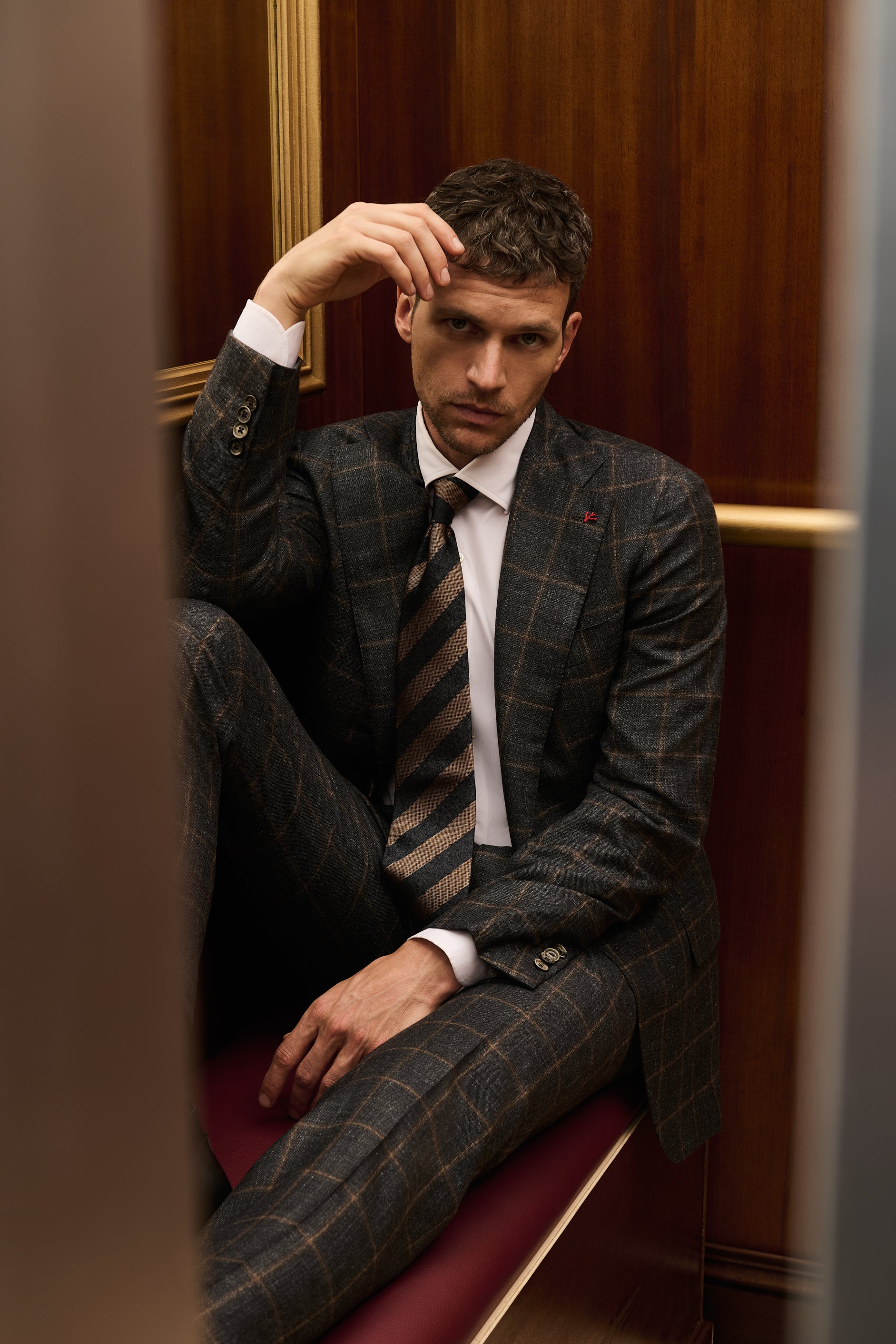 ISAIA Made to Measure: grey check suit with striped tie, seated on the elevator bench