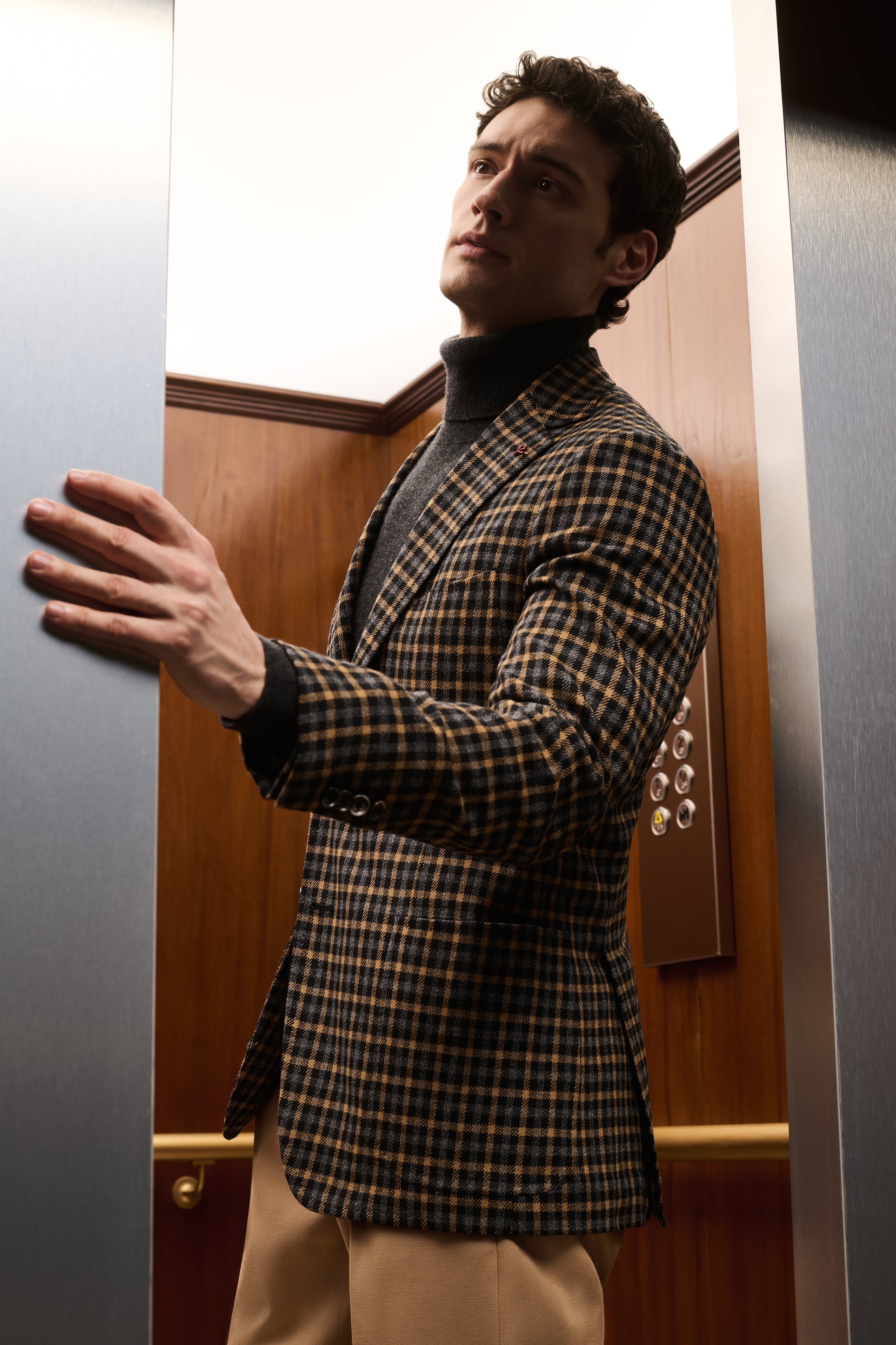 ISAIA Made to Measure: brown and mustard houndstooth jacket with black rollneck, a hand on the elevator door