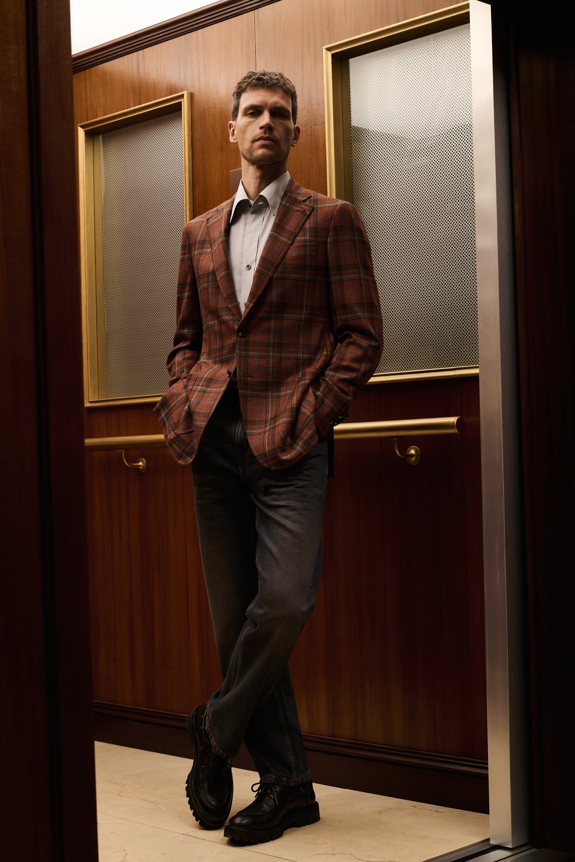 ISAIA Made to Measure: rust check jacket with grey trousers, legs crossed in the elevator