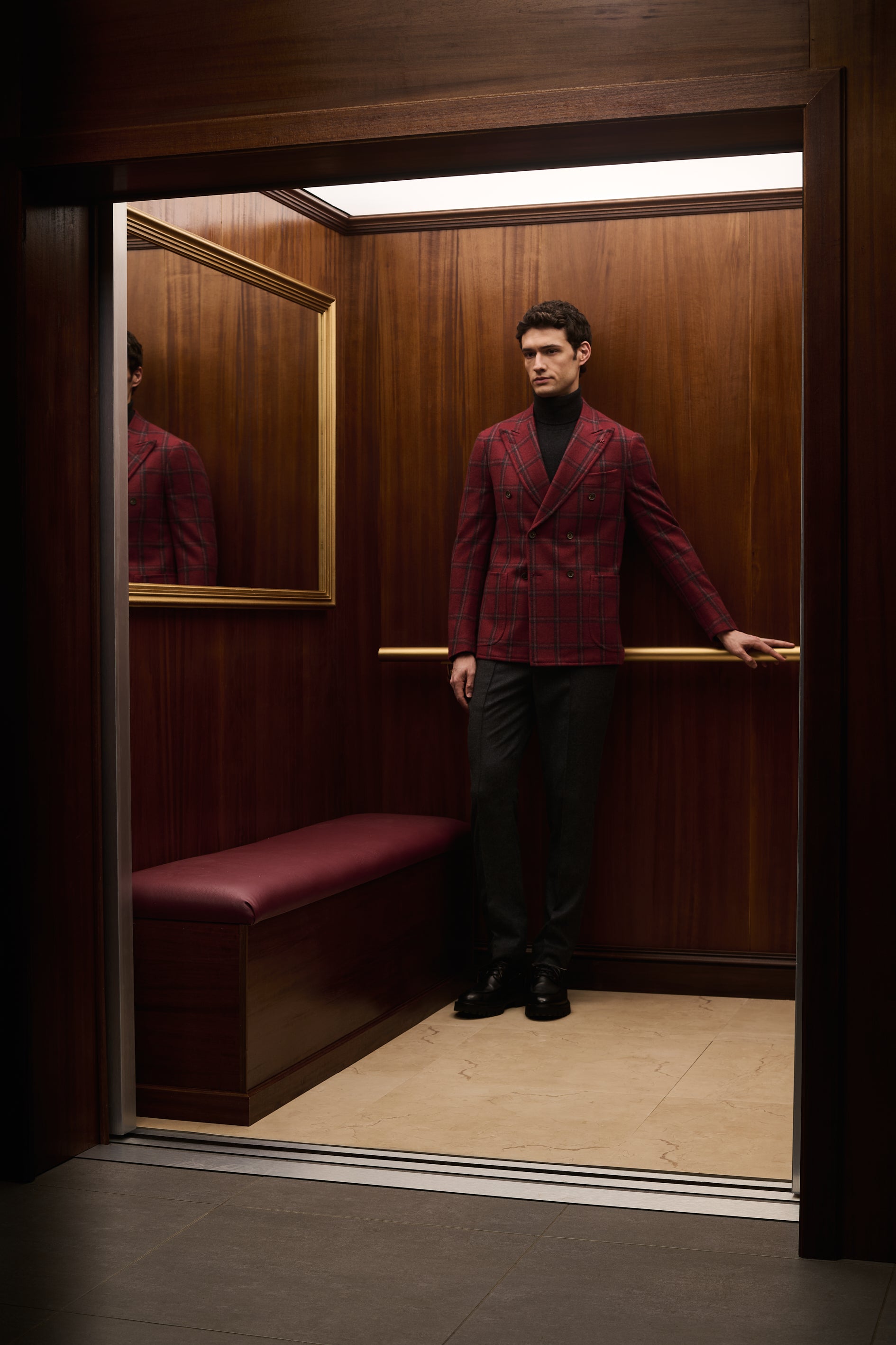 ISAIA Made to Measure: burgundy double-breasted jacket with black rollneck, seen through the open elevator doors
