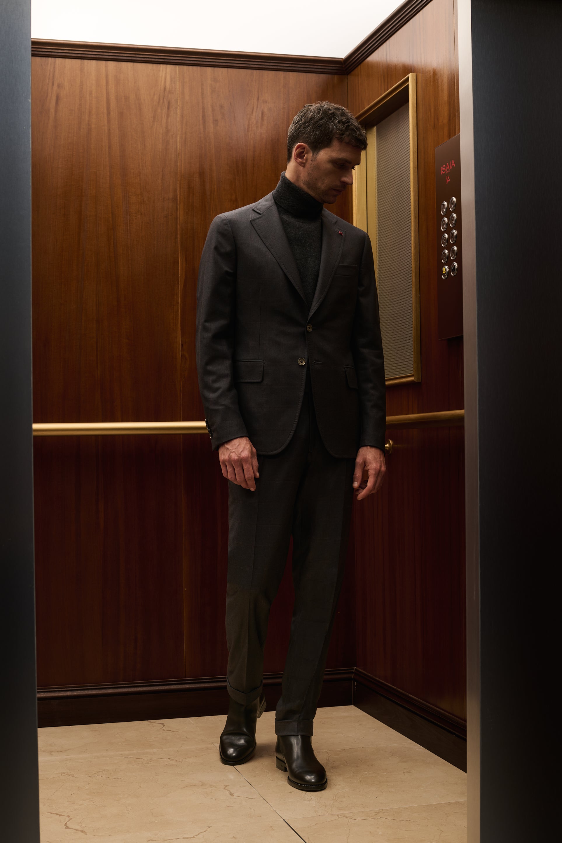 ISAIA Made to Measure: charcoal suit with black rollneck in a wood-panelled elevator